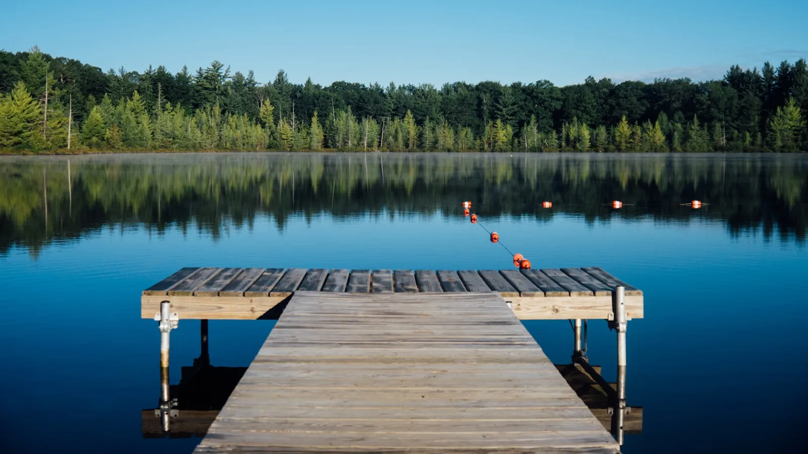A quiet wooden jetty reaching into a still forest lake at first light