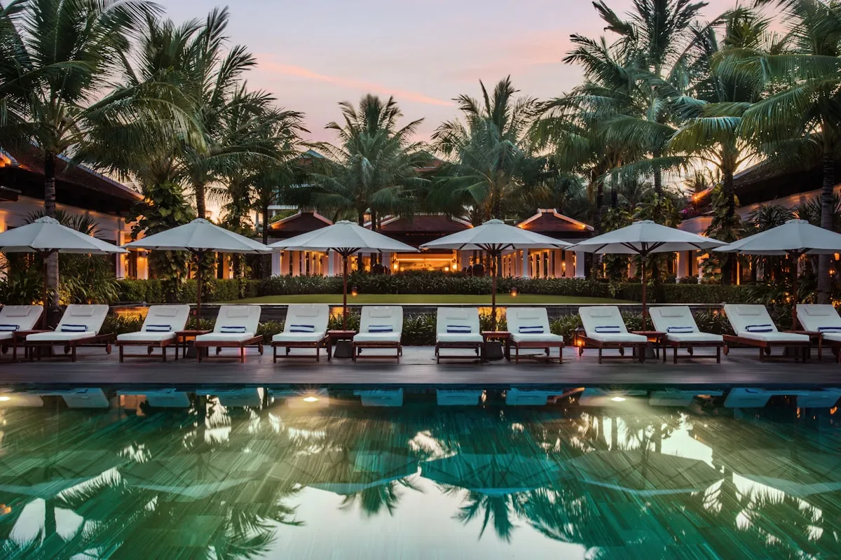 Palm-lined resort pool at dusk with a row of white loungers