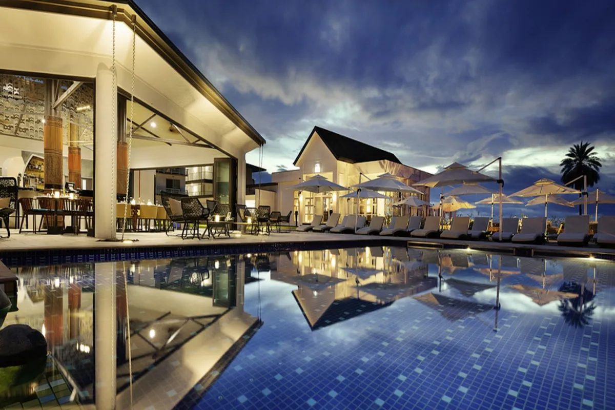 A resort restaurant terrace mirrored in a calm pool at blue hour